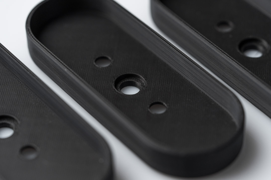 Detailansicht eines präzisen FDM 3D-Druck Bauteils aus schwarzem Kunststoff mit Bohrungen und sauberer Schichtstruktur