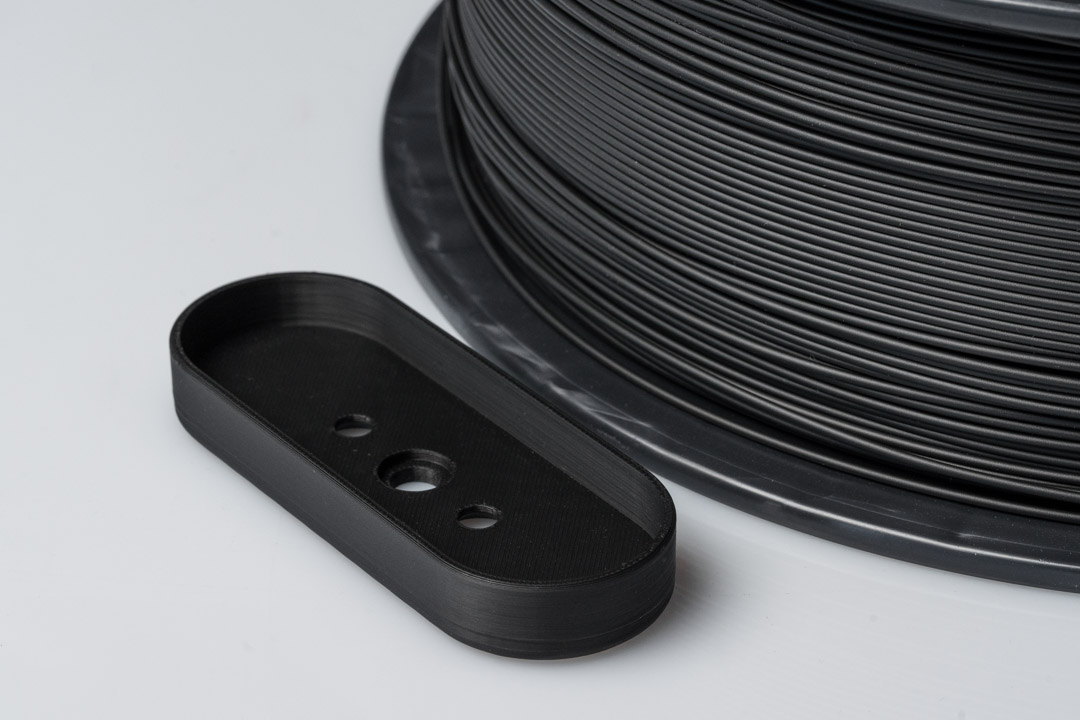 FDM-Bauteil aus additive Fertigungsverfahren neben Filamentrolle, eingesetzt im industriellen 3D-Druck