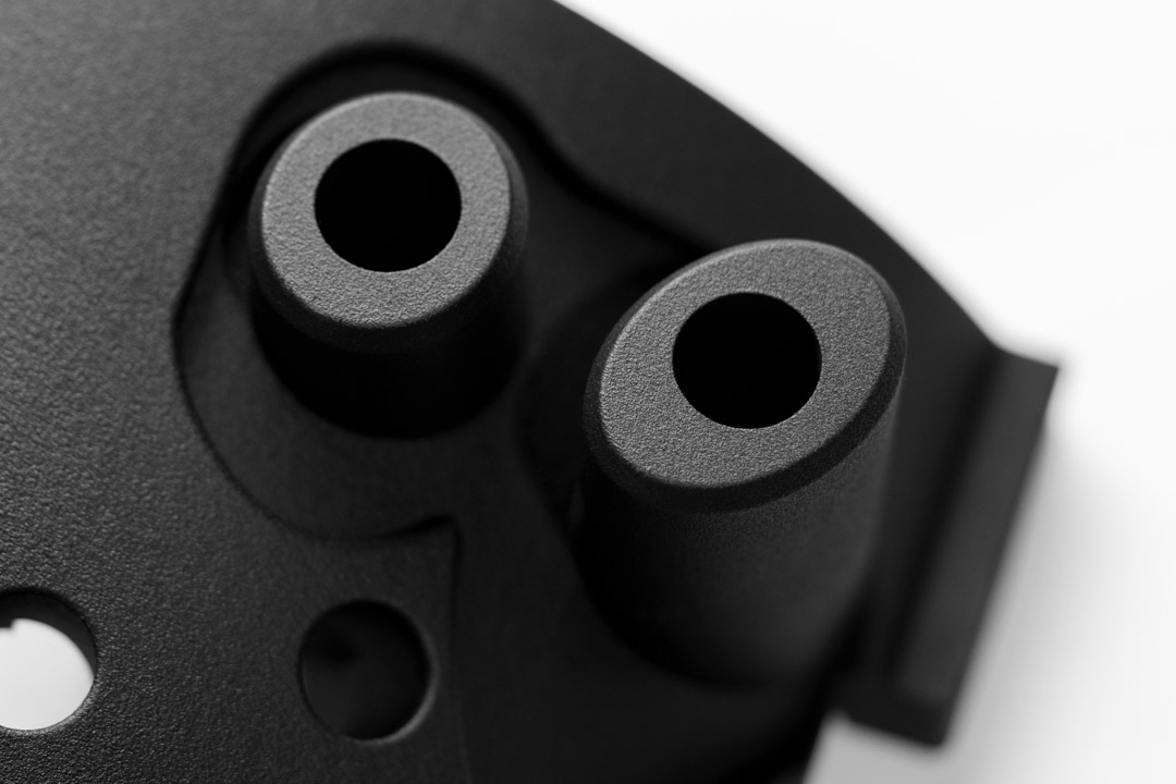 Detailaufnahme eines schwarzen, additiv gefertigten Kunststoffbauteils mit zwei zylindrischen Aufnahmen und präzisen Bohrungen – produziert durch Additive Fertigung für industrielle Anwendungen.
