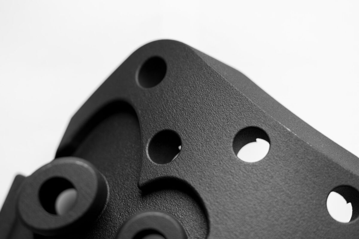 Schwarz gefärbtes DM60 Bauteil aus dem industrieller-3d-druck mit drei präzisen Bohrungen, klaren Konturen und sauberer, leicht strukturierter Oberfläche.