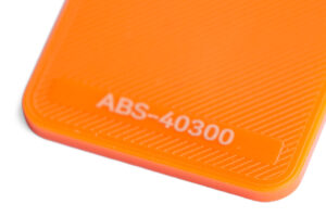 ABS 40300 - KIT3D GmbH – 3D-Technologie & Konstruktion Close-up of bright orange plastic with the text ABS-40300 on a rounded corner and diagonal texture.