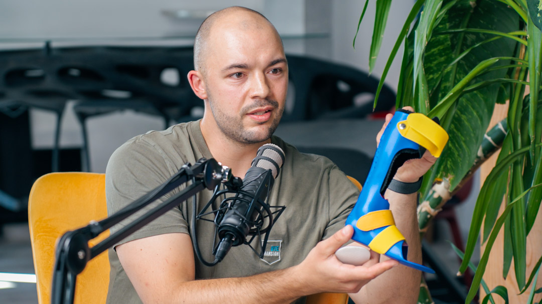 Emil zeigt im AdditiveTalk-Podcast eine blau-gelb gefärbte 3D-gedruckte Orthese als Beispiel für reproduzierbares Färben von Serienbauteilen.