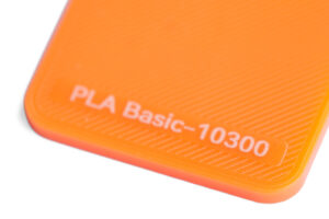PLA Basic 10300 - KIT3D GmbH – 3D-Technologie & Konstruktion Close-up of bright orange PLA plastic surface with the label 'PLA Basic-10300' visible at the corner.