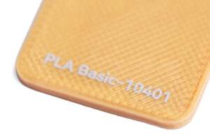 PLA Basic 10401 - KIT3D GmbH – 3D-Technologie & Konstruktion Close-up of an orange textured plastic piece with the text 'PLA Basic-10401' printed on it.