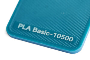 PLA Basic 10500 - KIT3D GmbH – 3D-Technologie & Konstruktion Close-up of a teal plastic surface with the embossed label 'PLA Basic-10500'.