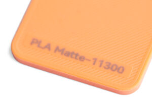 PLA Matte 11300 - KIT3D GmbH – 3D-Technologie & Konstruktion Close-up of an orange textured plastic piece with engraved text 'PLA Matte-11300'