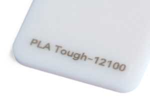 PLA Tough 12100 - KIT3D GmbH – 3D-Technologie & Konstruktion Close-up of a pale blue plastic surface with the engraving 'PLA Tough-12100' along the corner edge.