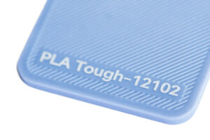 PLA Tough 12102 - KIT3D GmbH – 3D-Technologie & Konstruktion Close-up of a blue textured plastic surface with the embossed label 'PLA Tough-12102'.