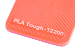 PLA Tough 12200 - KIT3D GmbH – 3D-Technologie & Konstruktion Close-up of an orange 3D-printed surface with diagonal grooves and the label 'PLA Tough-12200'