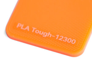 PLA Tough 12300 - KIT3D GmbH – 3D-Technologie & Konstruktion Close-up of an orange plastic surface labeled 'PLA Tough-12300' (3D printing filament type)