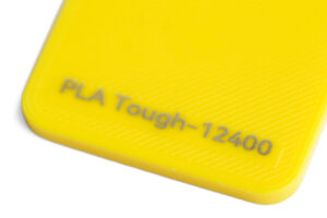 PLA Tough 12400 - KIT3D GmbH – 3D-Technologie & Konstruktion Close-up of a bright yellow surface with embossed text 'PLA Tough-12400'.