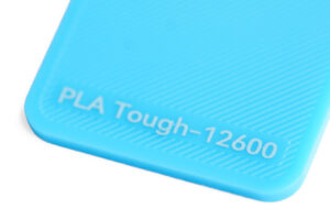 PLA Tough 12600 - KIT3D GmbH – 3D-Technologie & Konstruktion Close-up of a bright blue object with 'PLA Tough-12600' embossed on it, likely a 3D printing material label appraised surface color.